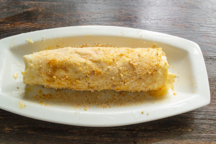 Coating the egg-washed roll with breadcrumbs for a crispy crust A hand sprinkling breadcrumbs over the egg-coated lavash roll.