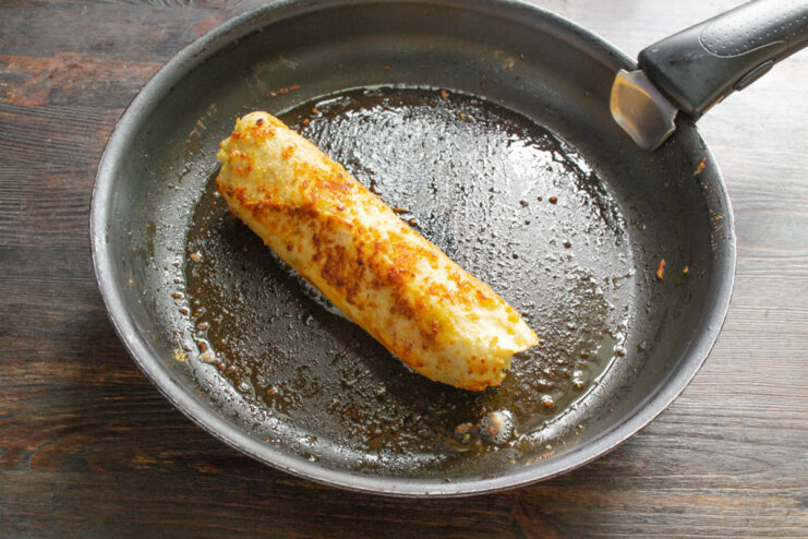 Frying the 3 cheese lavash roll until perfectly golden The breaded lavash roll being fried in a pan with hot oil until golden brown.