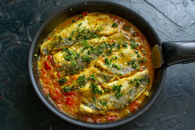 A hand sprinkling freshly chopped cilantro over the cooked Moroccan-style fish in a pan.