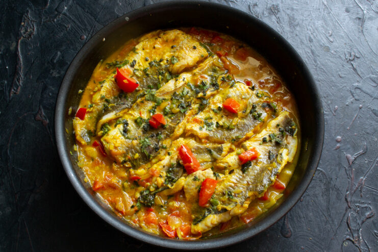 A serving of Moroccan-style fish on a plate with a side of fresh bread for dipping in the sauce.