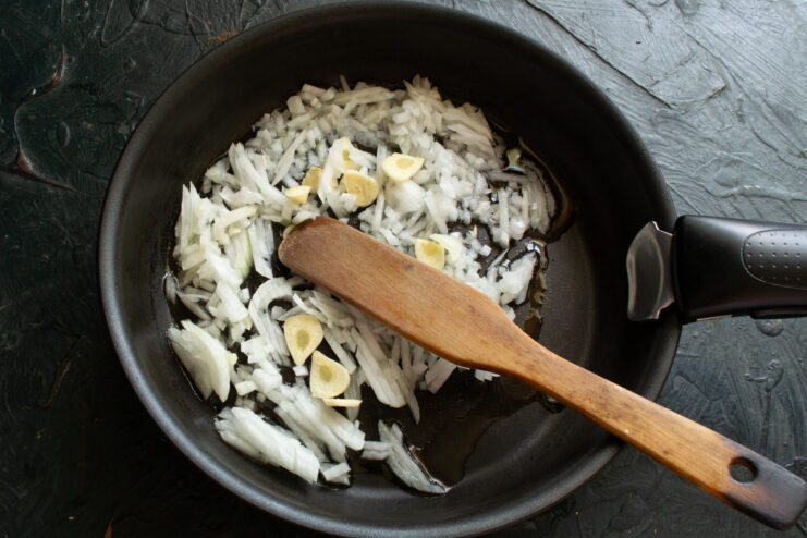 A cutting board with finely chopped onions and thinly sliced garlic cloves.