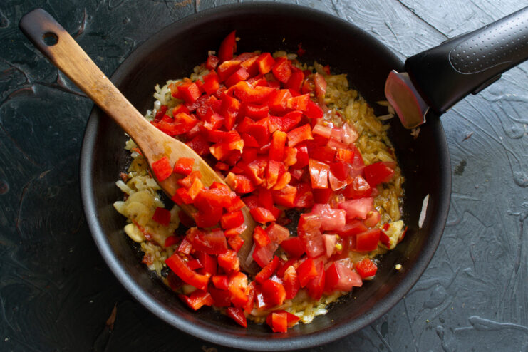 Chopped tomatoes and bell peppers being added to the skillet with spices.