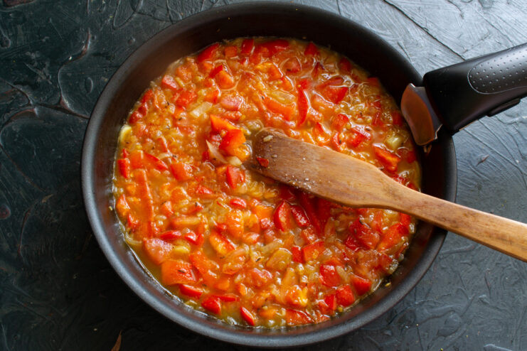 Water being poured into a pan with sautéed vegetables to create a sauce.