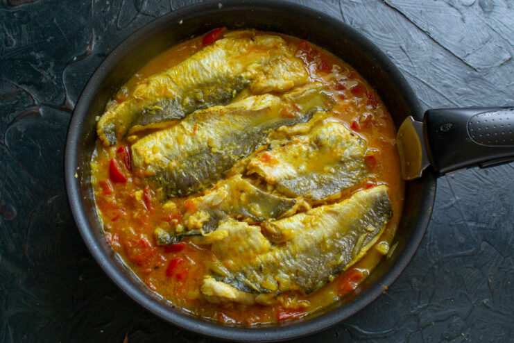 Fish fillets simmering gently in the sauce in an uncovered pan.
