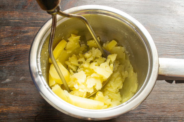 Preparing the potato base for the fish patties by mashing it with butter. A bowl of freshly mashed potatoes with a piece of butter melting on top.