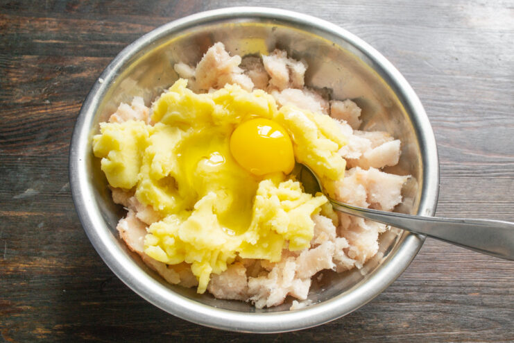 Adding an egg to the fish and potato mixture to bind the patties. An egg being cracked into a bowl with the fish and potato mixture.