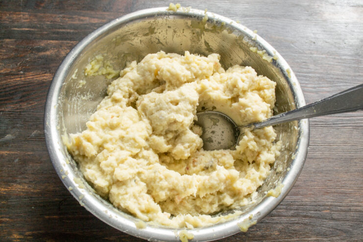 Thoroughly mixing the fish patty ingredients for a smooth, consistent texture. Hands mixing the fish, potato, and egg mixture in a bowl.