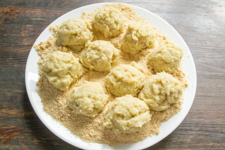 Shaping the fish and potato mixture into small, round patties before cooking. Hands shaping the fish and potato mixture into a small, round patty.