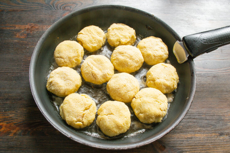Placing the breaded fish patties into a hot skillet to start frying. Several breaded fish patties being placed into a hot, oiled frying pan.