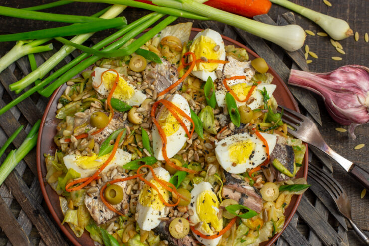 A bowl of finished Fish Salad with Saury and Olives, garnished with herbs and egg wedges.