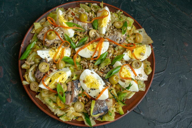 The final presentation of the delicious saury and olive fish salad. The finished fish salad with saury and olives, garnished with black pepper and green onions, ready to be served.