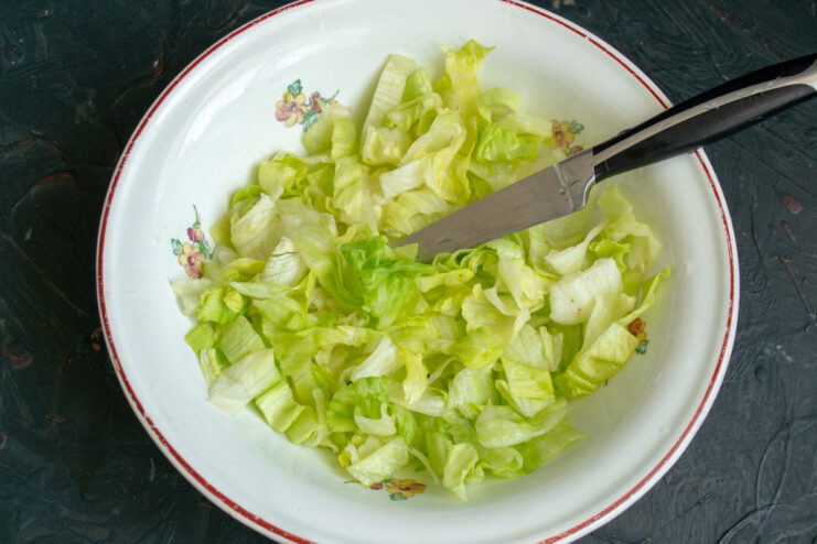 Step 1: Preparing the lettuce base for the fish salad. A close-up shot of iceberg lettuce being chopped into wide strips on a cutting board.
