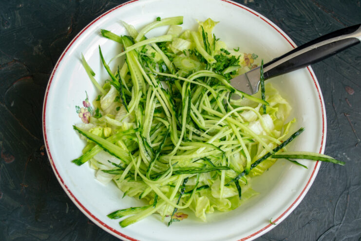 How to julienne cucumber for a perfect salad texture. A fresh cucumber being cut into thin julienne strips on a cutting board.