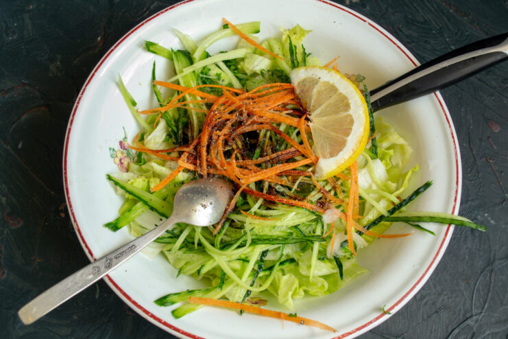 Preparing carrots for the salad: fresh or Korean-style. Julienned carrots being added to the bowl with other salad ingredients.