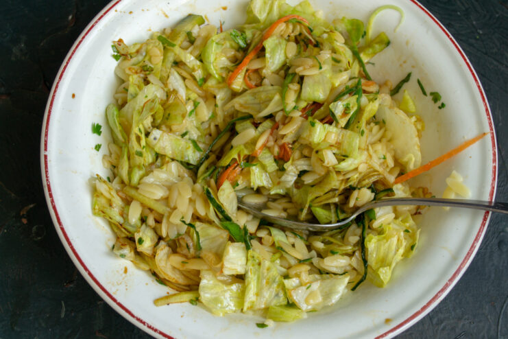 Combining cooked pasta with the fresh vegetable mix. Cooked and cooled small pasta being added to a bowl of chopped vegetables.