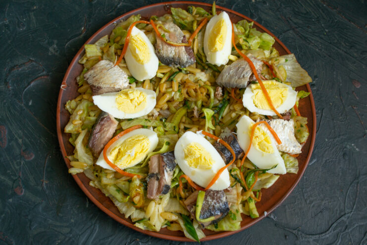 Garnishing the salad with perfectly cooked hard-boiled eggs. Hard-boiled egg wedges being arranged in the salad bowl next to the saury.
