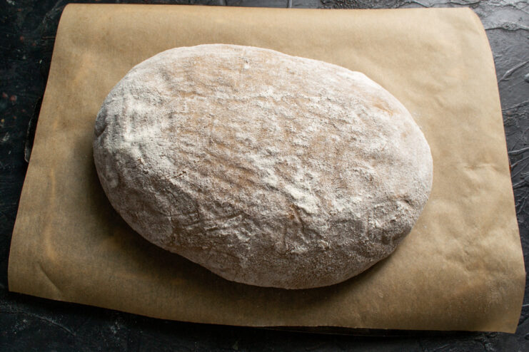 Turning Out the Proofed Loaf for Baking A fully proofed rye sourdough loaf turned out of its basket onto parchment paper, ready to be scored.