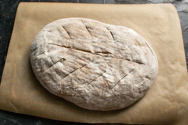 Scoring the Bread Before Baking Scoring the top of the sourdough rye loaf with a blade to control its expansion in the oven.