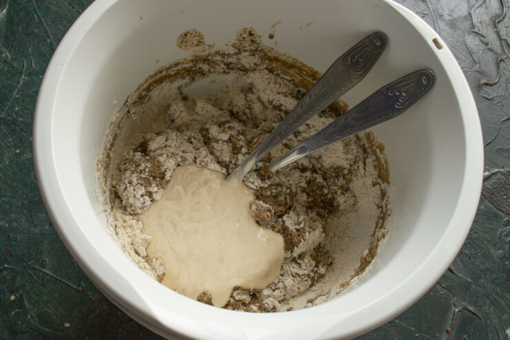 Adding the Active Sourdough Starter Adding a bubbly, active sourdough starter to the bread dough mixture in a bowl.