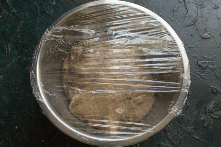 Covering the Dough to Proof A bowl of dough covered tightly with plastic wrap, ready for bulk fermentation.