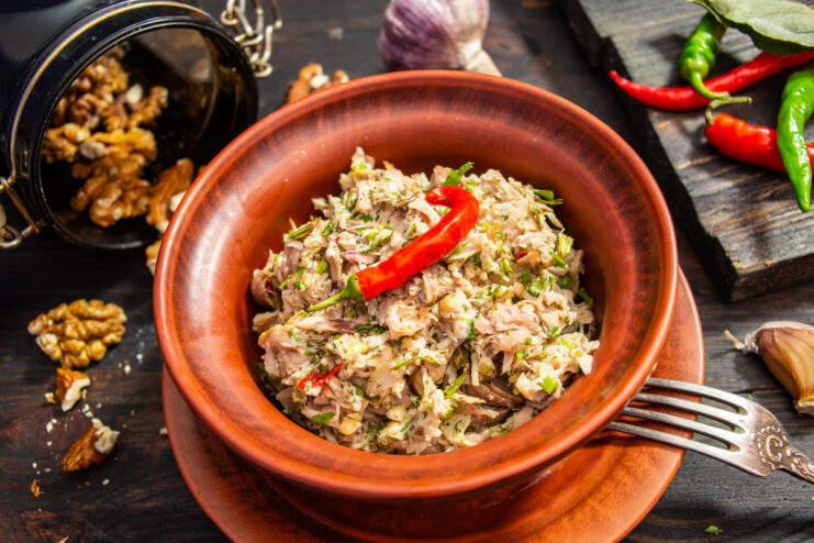 A bowl of chicken and walnut salad, garnished with fresh herbs and chili pepper.