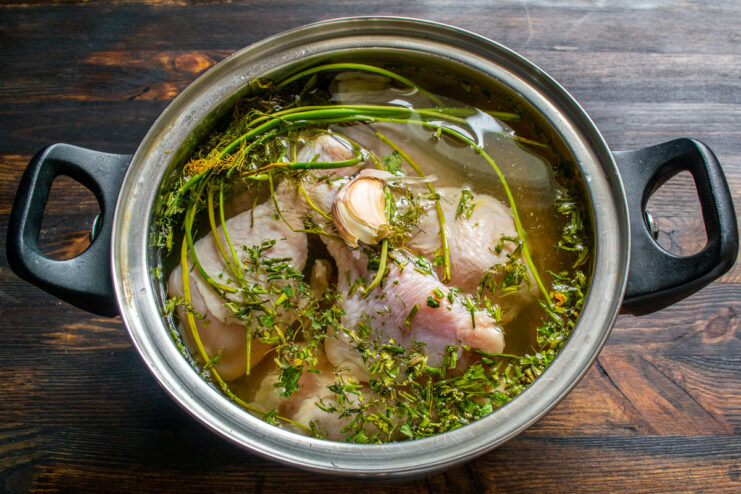 How to Perfectly Poach Chicken for Salad Chicken drumsticks simmering in a pot with broth ingredients like onion and herbs.