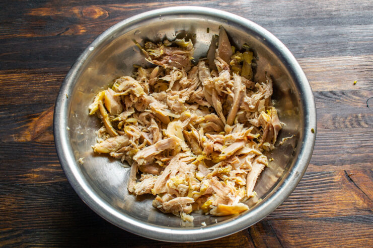 Shredding Cooked Chicken for the Salad Shredded chicken meat in a bowl, separated from the bones.