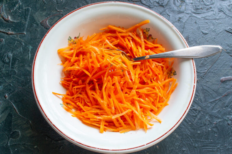 Grating fresh carrots for the salad base. Freshly grated carrots in a bowl, the first step of the salad preparation.