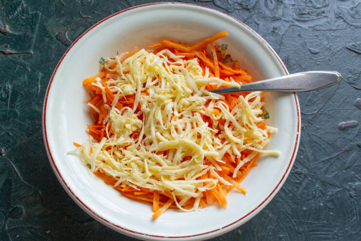 Adding grated cheese to the carrots for a savory flavor. Grated cheese being added to a bowl of grated carrots.