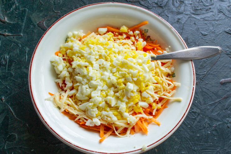 Adding chopped hard-boiled eggs for protein and texture. Finely chopped hard-boiled eggs being added to the carrot and cheese mixture.