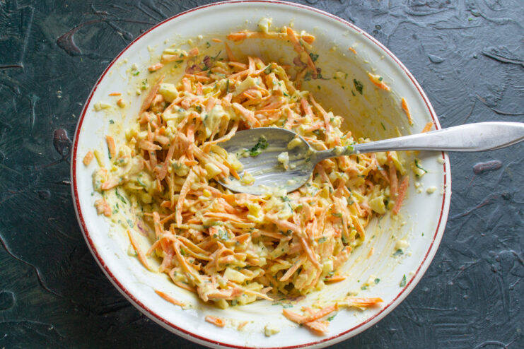 Mixing the salad with mayonnaise to create a creamy dressing. Mayonnaise being added to the carrot, cheese, and egg salad.