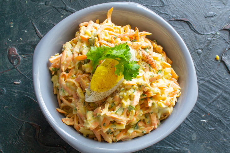 The finished carrot salad, beautifully garnished and ready to serve. The finished carrot salad with cheese and egg in a serving bowl, garnished with egg and parsley.