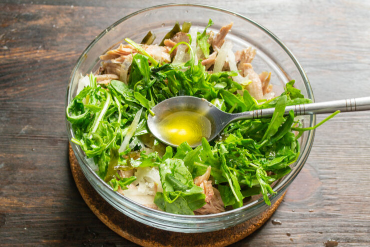 Step 5: Seasoning the Salad with Salt and Olive Oil Olive oil being drizzled over the salad ingredients in a bowl.