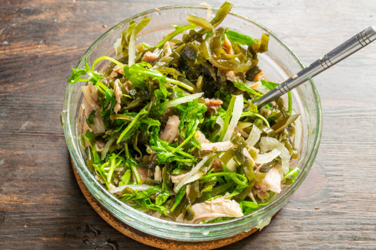 Step 7: Tossing the Salad to Combine Flavors Mixing the seaweed, chicken, and arugula salad in a bowl with a spoon.