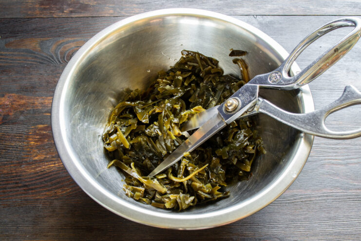 Preparing the seaweed for the salad Cutting canned seaweed with kitchen scissors in a glass bowl.