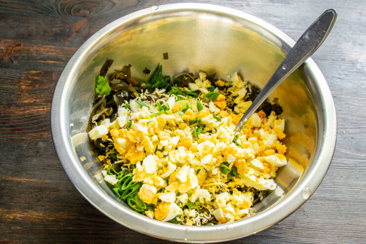Adding diced hard-boiled eggs for protein Adding diced hard-boiled eggs to the salad mixture in a bowl.
