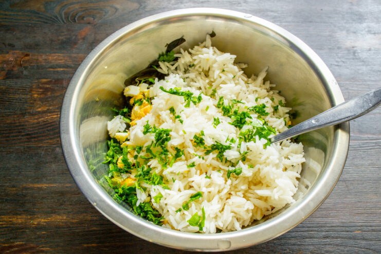 Combining cooked rice with the other salad ingredients Adding cooled cooked rice to the bowl with seaweed and other ingredients.