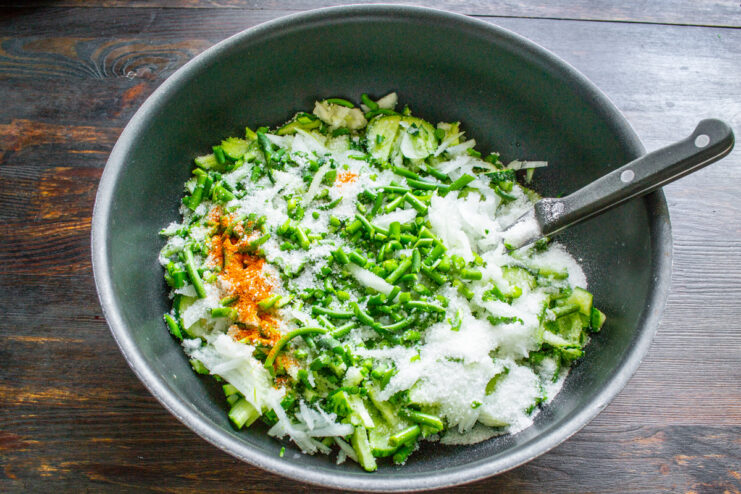 Seasoning the Salad with Salt, Sugar, and Spice Adding salt, sugar, and red pepper to the bowl of chopped vegetables.