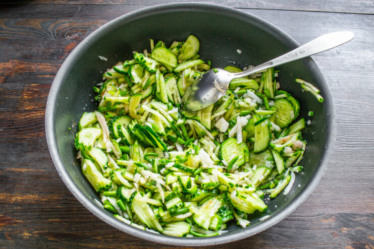 Letting the Vegetables Macerate to Create a Natural Brine A large pot with mixed cucumbers, onions, and garlic scapes marinating to release juices.