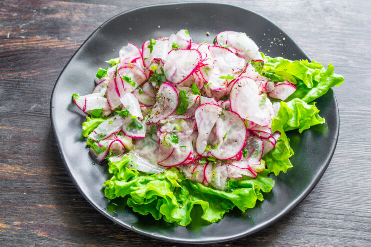 Serving the Fresh Radish Salad on a Bed of Lettuce A finished plate of radish and herb salad served on a bed of green lettuce, seasoned with black pepper.