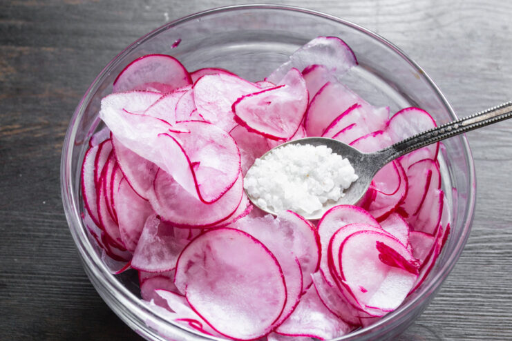 Salting the Radishes to Mellow Their Flavor Thinly sliced radishes in a bowl, mixed with coarse sea salt.