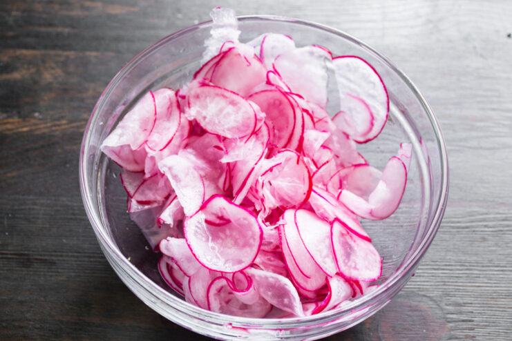 Rinsing the Salted Radishes in a Colander Rinsing salted radish slices in a white colander under running water.