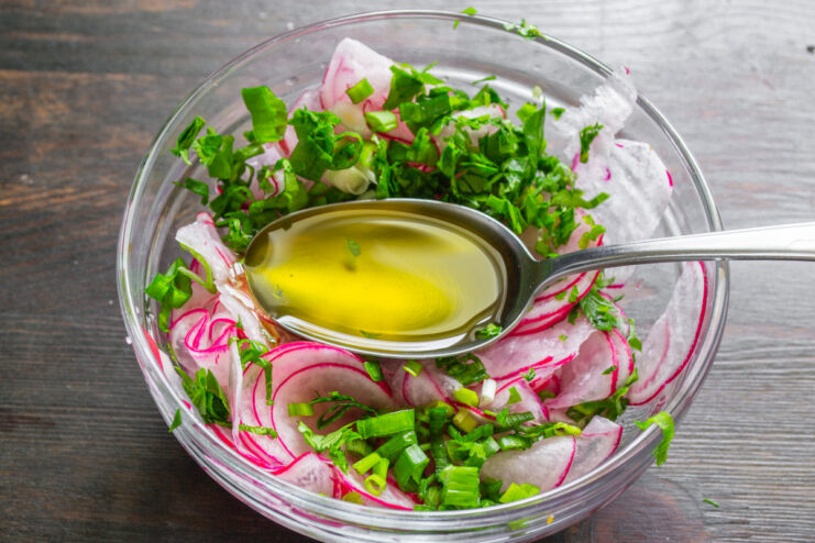 Dressing the Salad with Extra Virgin Olive Oil Pouring extra virgin olive oil from a bottle into the bowl of radish salad.