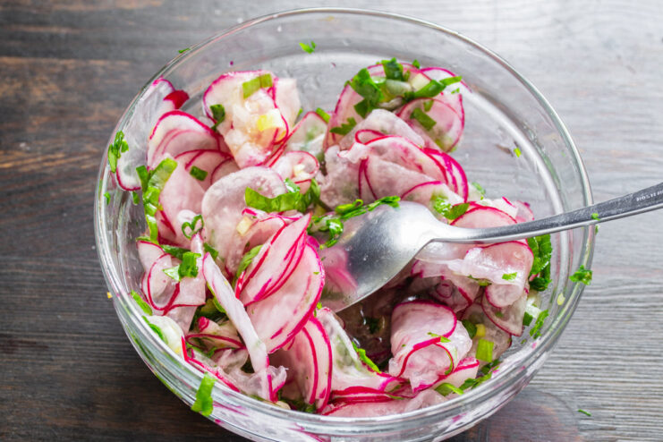 Tossing the Radish Salad to Combine All Ingredients Tossing the radish, green onion, and parsley salad in a bowl with a spoon.