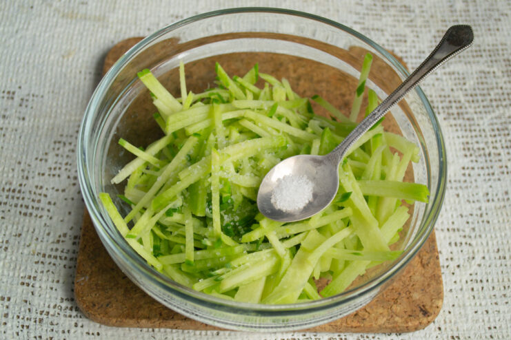 Grating the radish and seasoning with sea salt. Grated green radish in a bowl being mixed with sea salt.