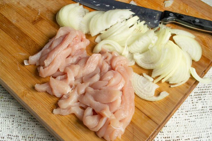 Slicing the chicken breast into thin strips. Chicken breast fillet being sliced into thin strips on a cutting board.
