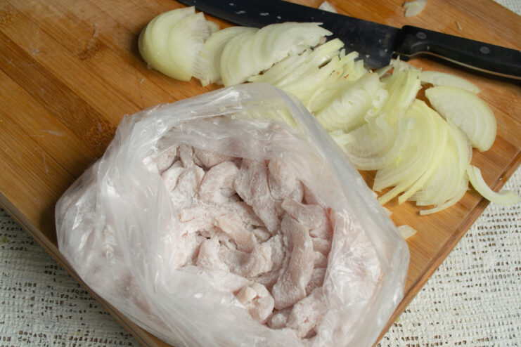 Coating the chicken strips in cornstarch using a bag. Shaking chicken strips with cornstarch in a sealed plastic bag.