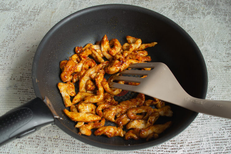 Frying the starch-coated chicken fillet. Starch-coated chicken strips being added to a hot wok with oil.