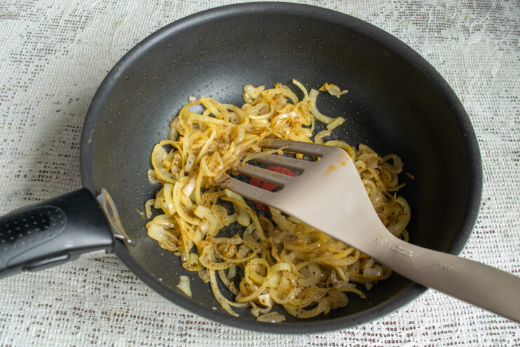 Sautéing the sliced onions in the same pan. Sliced onions being sautéed in a wok.