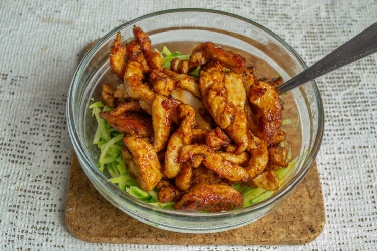 Combining the radish and cooked chicken. Cooked chicken strips being added to a bowl of grated green radish.